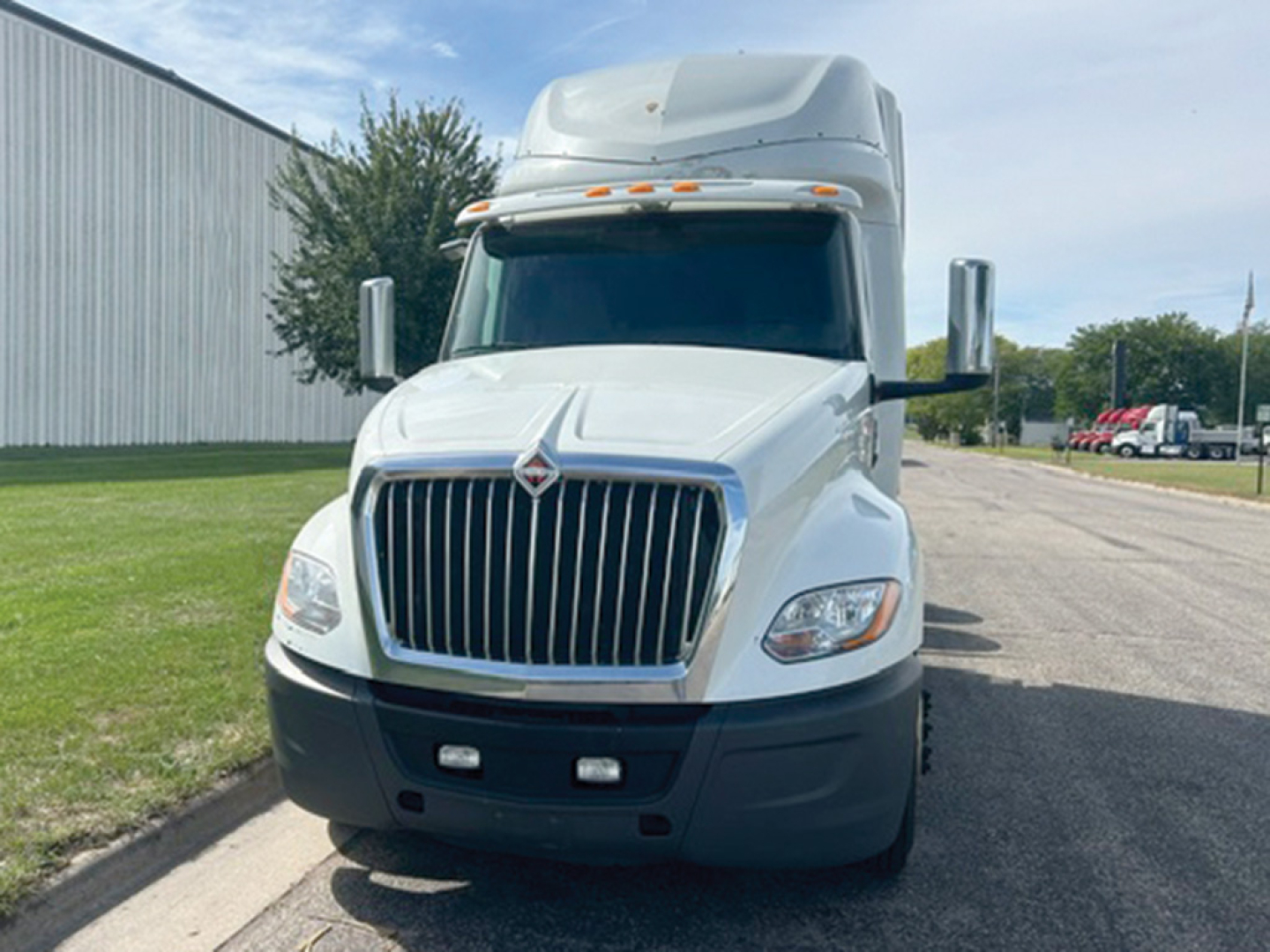 Truck cab front view showing International LT625 with large vertical grille, white paint, black bumper, and aerodynamic mirrors.