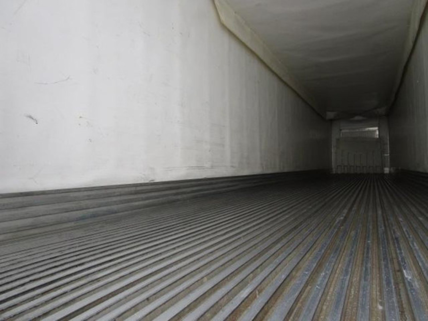 Trailer interior cargo area showing ribbed metal floor and white walls, empty with distant rear doors.