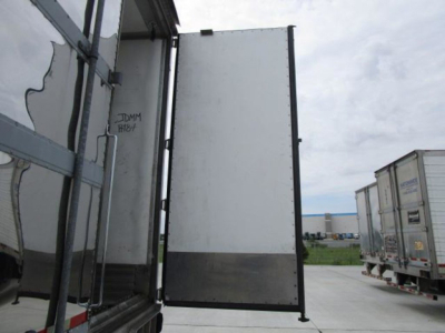 Refrigerated trailer door open showing interior panels and exterior body in a yard with other trailers nearby.