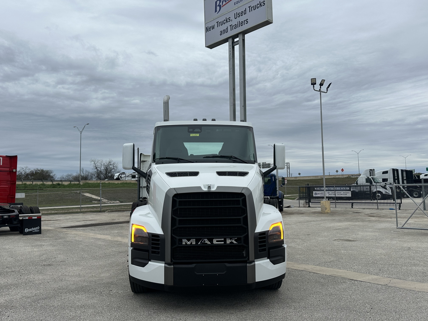 Truck front view of a white 2026 Mack PR64T daycab showing headlights and grille with Mack lettering.