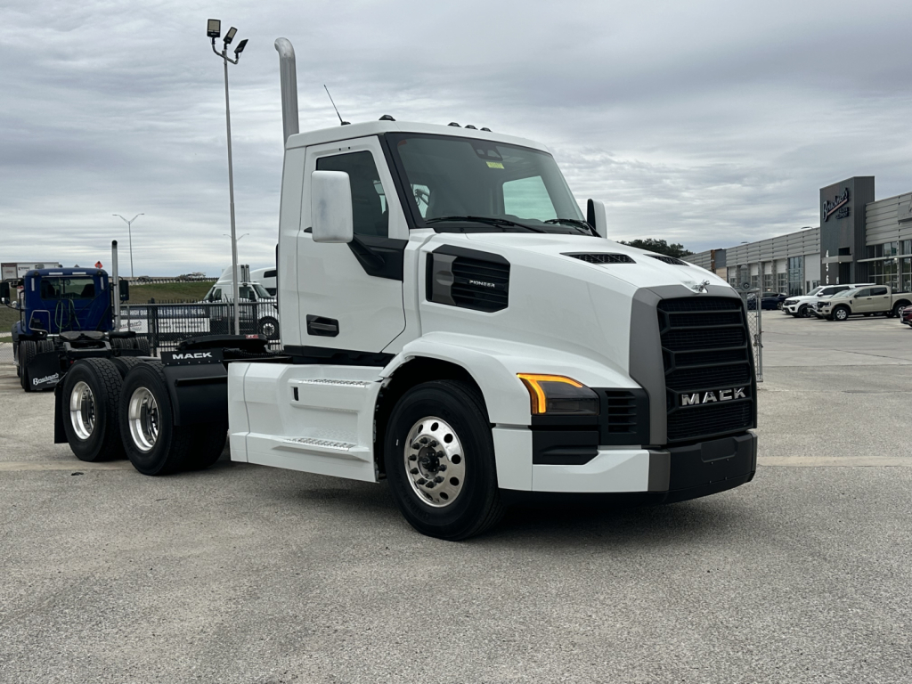 Mack PR64T conventional daycab truck side view showing white cab, black grille, dual rear axles, and chrome fuel tanks.