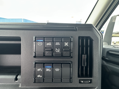 Dashboard control panel in a Mack PR64T showing switches and indicator icons; visible are multiple square buttons with symbols including trailer/vehicle functions, and an air vent to the right.