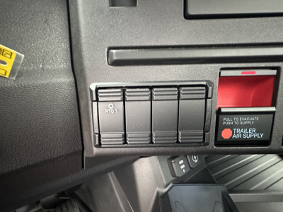 Dashboard control panel view showing left-side PTO switch labeled PTO 1 and a red trailer air supply switch with text 'PULL TO EVACUATE PUSH TO SUPPLY' in a Mack PR64T cab.