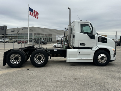 Truck chassis side view showing Mack PR64T cab with white exterior, dual rear axles, and exposed frame rails; no body attached in rear.