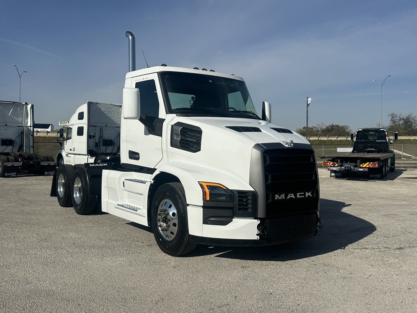 Mack PR64T conventional daycab truck in white parked in lot, front three-quarter view.