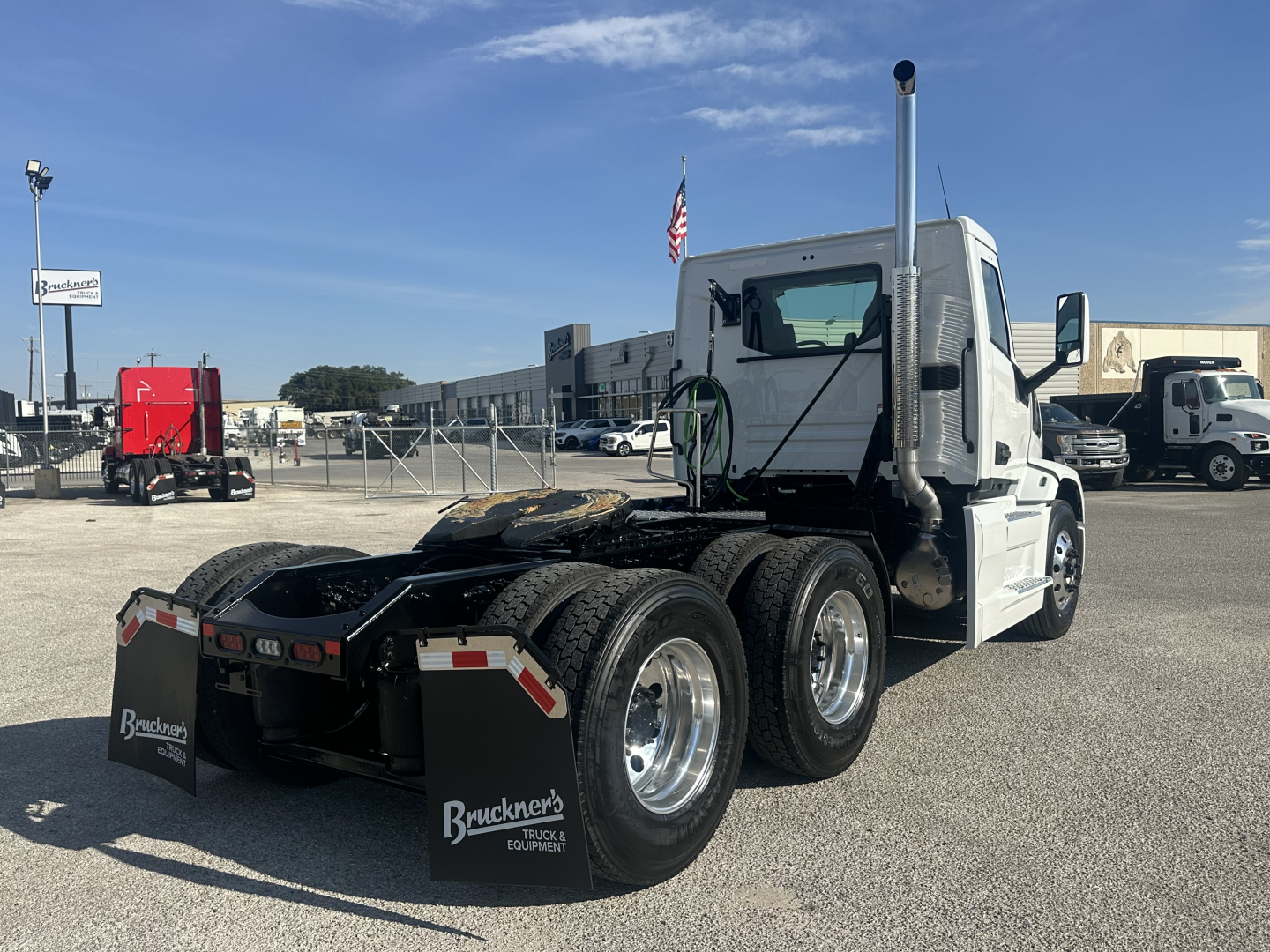 Mack PR64T conventional daycab truck chassis rear view showing five wheels and vertical exhaust, in a truck lot with blue sky.
