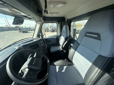 Mack PR64T truck cab interior showing steering wheel, driver seat with Mack logo, and passenger seat in light gray and black upholstery.