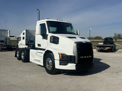 Mack PR64T conventional daycab truck in white parked in lot, front three-quarter view.