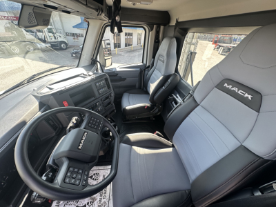 Mack PR64T truck cab interior showing steering wheel, dashboard, and gray leather seats with Mack logo.