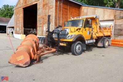 Industrial front view of a yellow 2011 International WorkStar 7400 dump plow truck with a large orange snow plow attached, in a yard next to a wooden building.