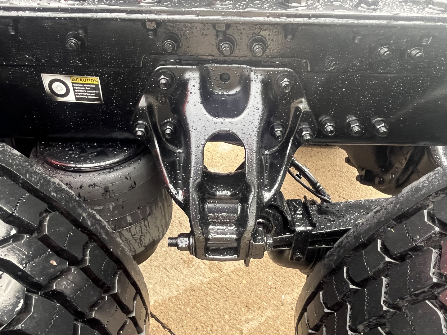 Truck rear undercarriage showing suspension hanger and leaf springs, with a sticker and VIN plate area visible.