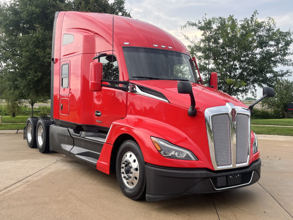 Kenworth T680 sleeper tractor in red, front-left view showing large grille, aerodynamic hood, side mirrors, and dual rear axles.