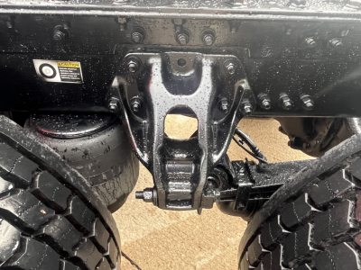 Truck rear undercarriage showing suspension hanger and leaf springs, with a sticker and VIN plate area visible.