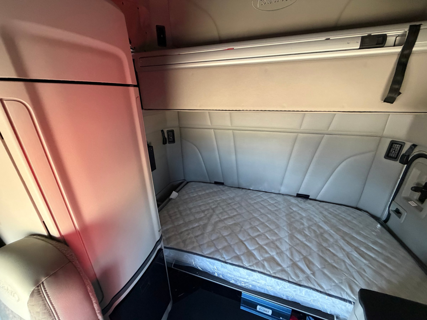 Peterbilt truck sleeper cab interior showing a quilted mattress in the bunk area with side storage and paneling.