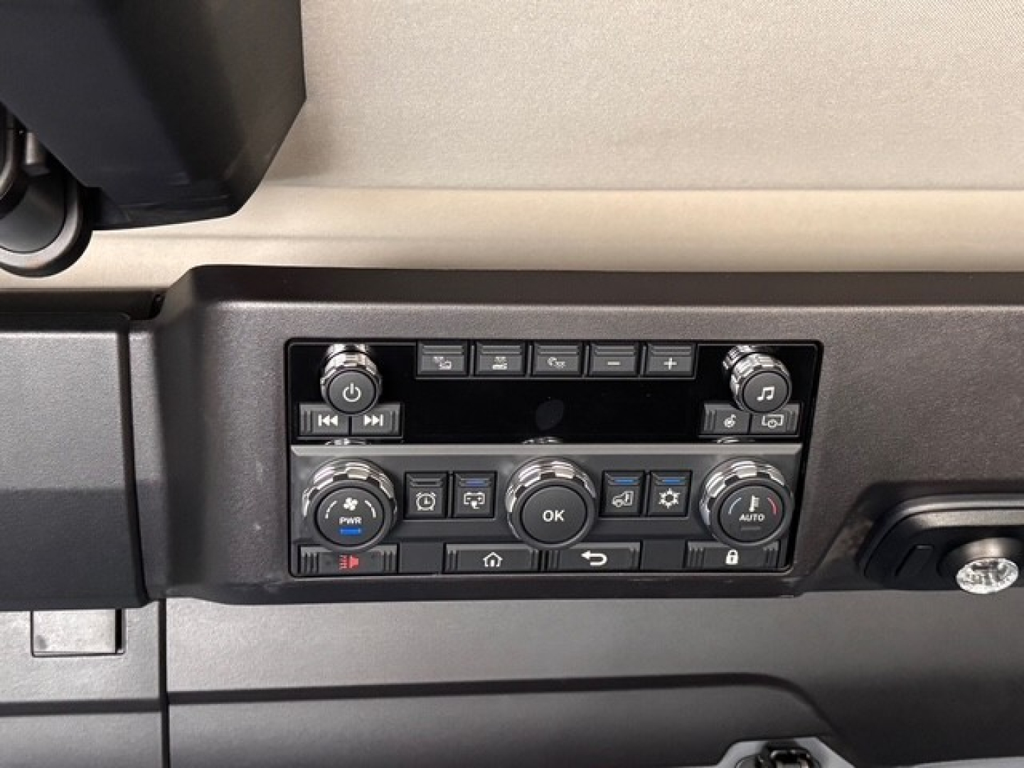 Trucks dashboard control panel showing various climate and media buttons, two round knobs on either side, and a central OK button.