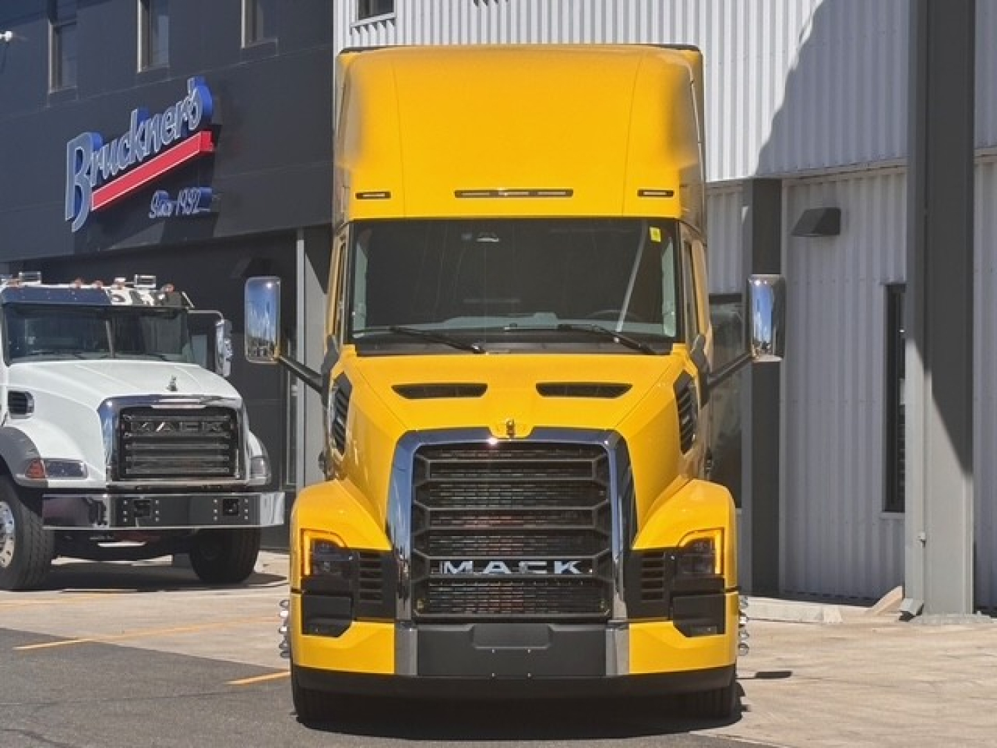 New yellow Mack PR64T76H conventional sleeper truck front view with large grille and chrome accents.