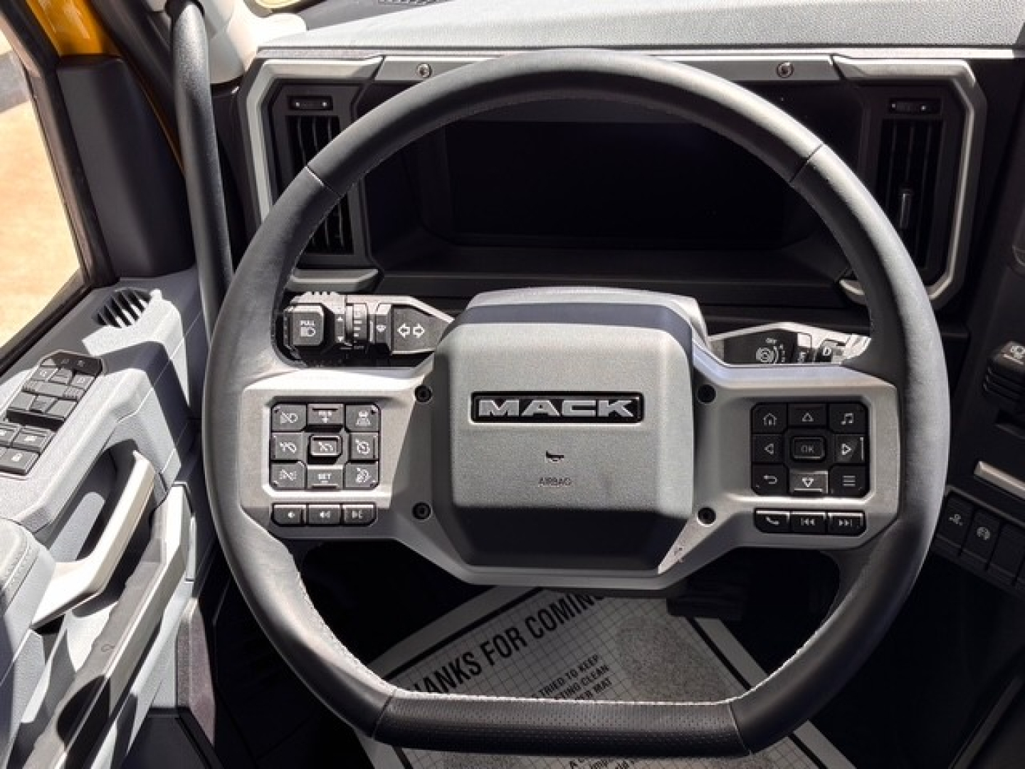 Mack truck steering wheel with many control buttons in center; dashboard visible in background.