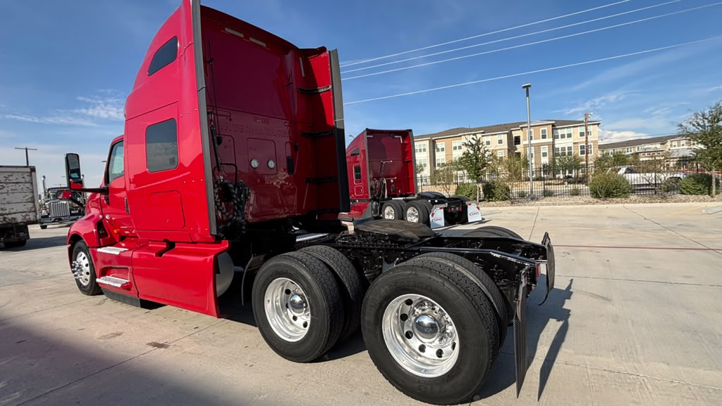 Truck chassis with red cab and dual rear axles, side view showing cab back and 6-wheel arrangement.