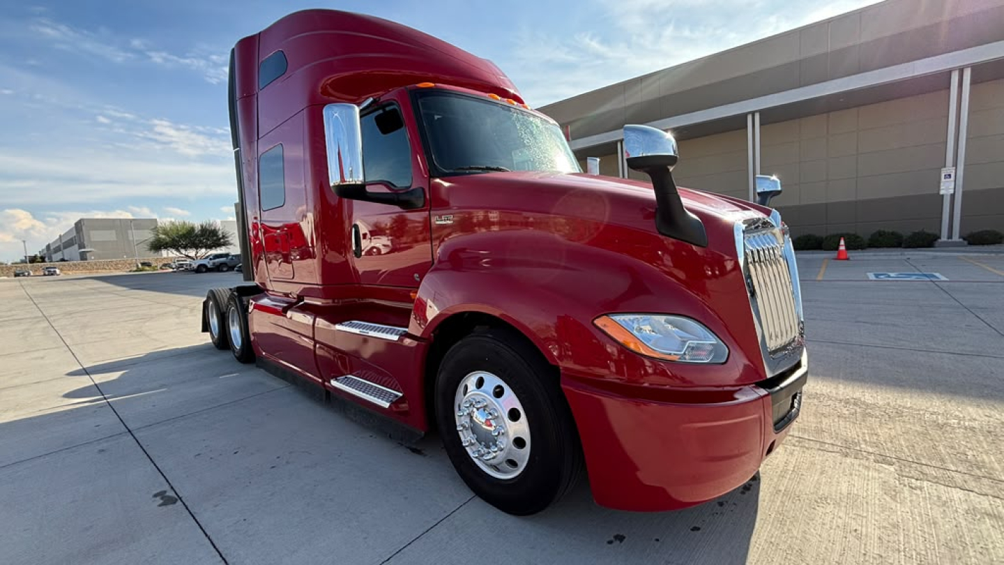 Truck cab exterior showing red 2022 International LT625 tractor with chrome grille, side mirrors, and sleeper cab, front-left angle.