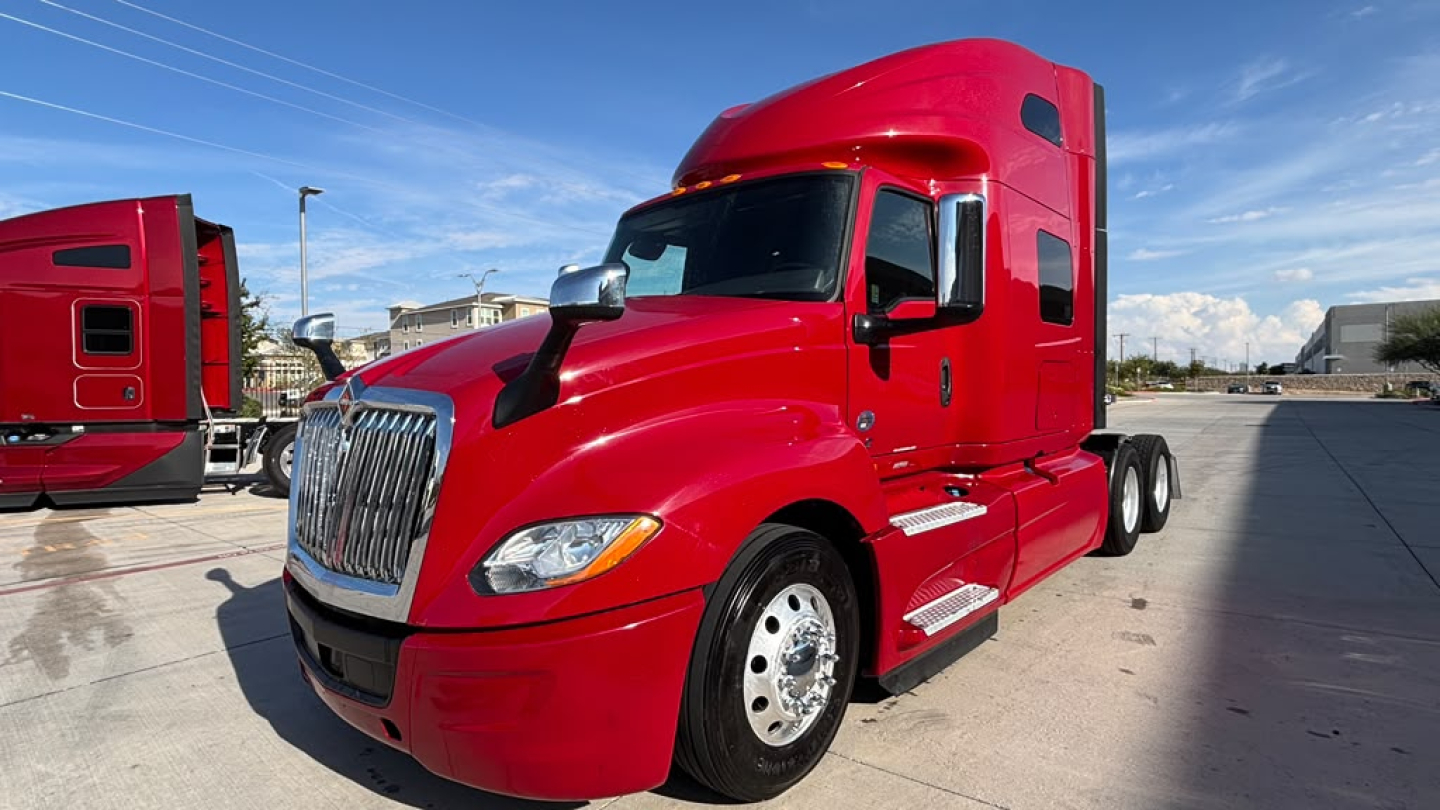 Red International LT625 semi-truck tractor in a parking lot, side view showing cab with aerodynamic mirrors and chrome grille.