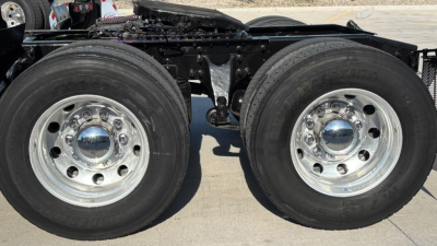 Truck drivetrain showing dual rear wheels with chrome hubcaps and suspension; portion of frame and fuel lines visible