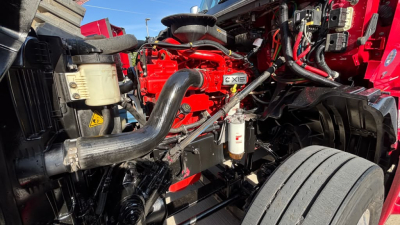 Truck engine bay showing red International LT625 with drivetrain components, hoses, and air filter housing visible.