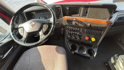Truck interior dashboard of a 2022 International LT625 showing steering wheel, center console with controls, wood trim, and cup holders.