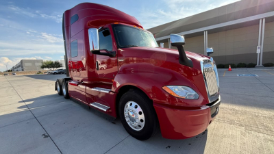 Truck cab exterior showing red 2022 International LT625 tractor with chrome grille, side mirrors, and sleeper cab, front-left angle.