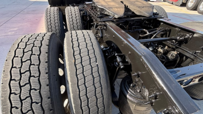 Truck chassis with dual rear axles and heavy-duty tires; engine bay area shows black painted frame and components.