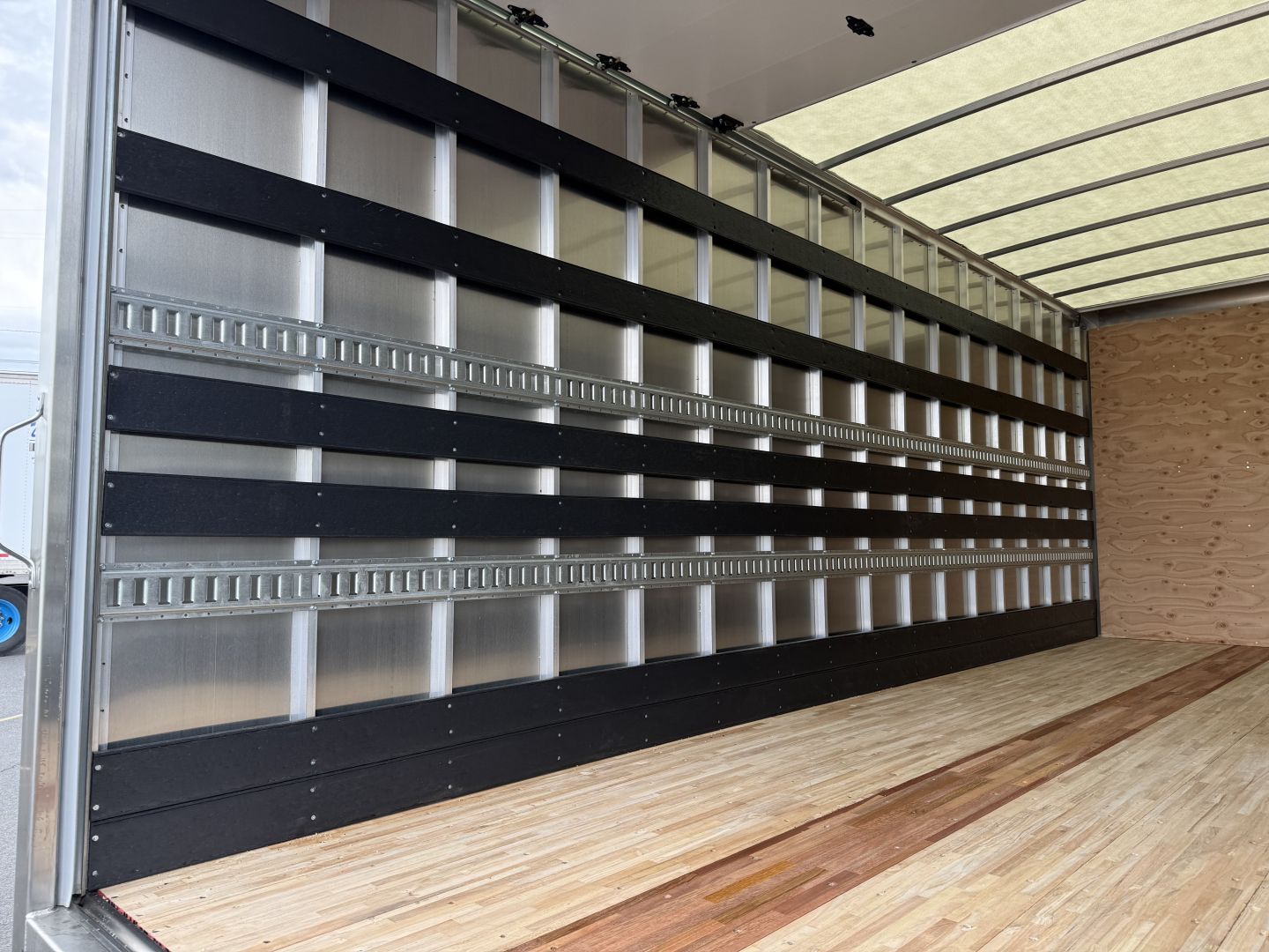 Isuzu NQR box truck interior with wooden cargo floor and metal side panels with black horizontal rails.