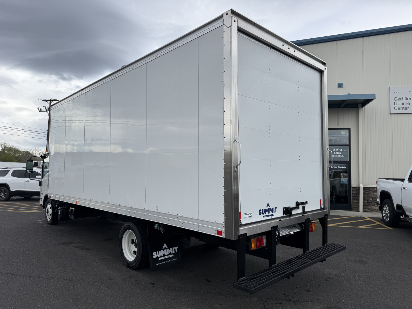 Box truck rear and side view with Isuzu NQR, aluminum cargo trailer, Summit rear stairs, white cargo body, black chassis, dock area background.