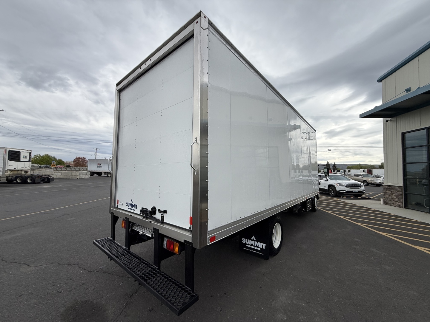 Isuzu box truck rear-right view showing white box body and black metal stairs; Summit branded wheel well and rear bumper visible.