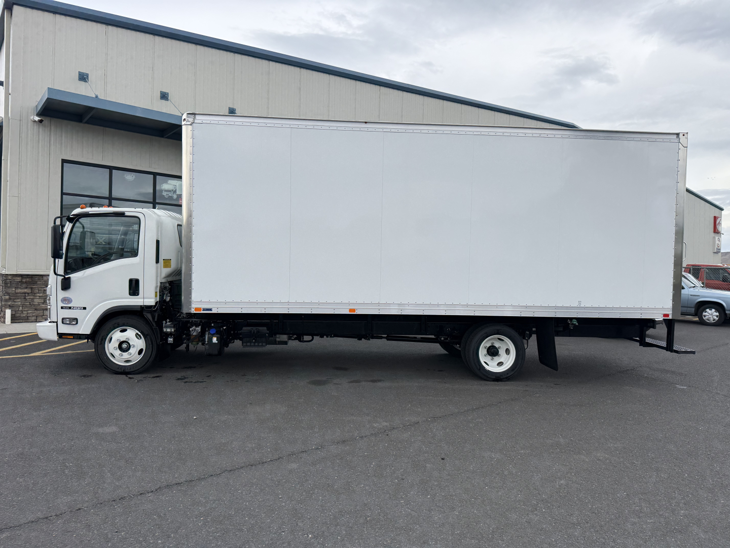 Isuzu NQR box truck side view showing cargo box and cab in a dealership lot.