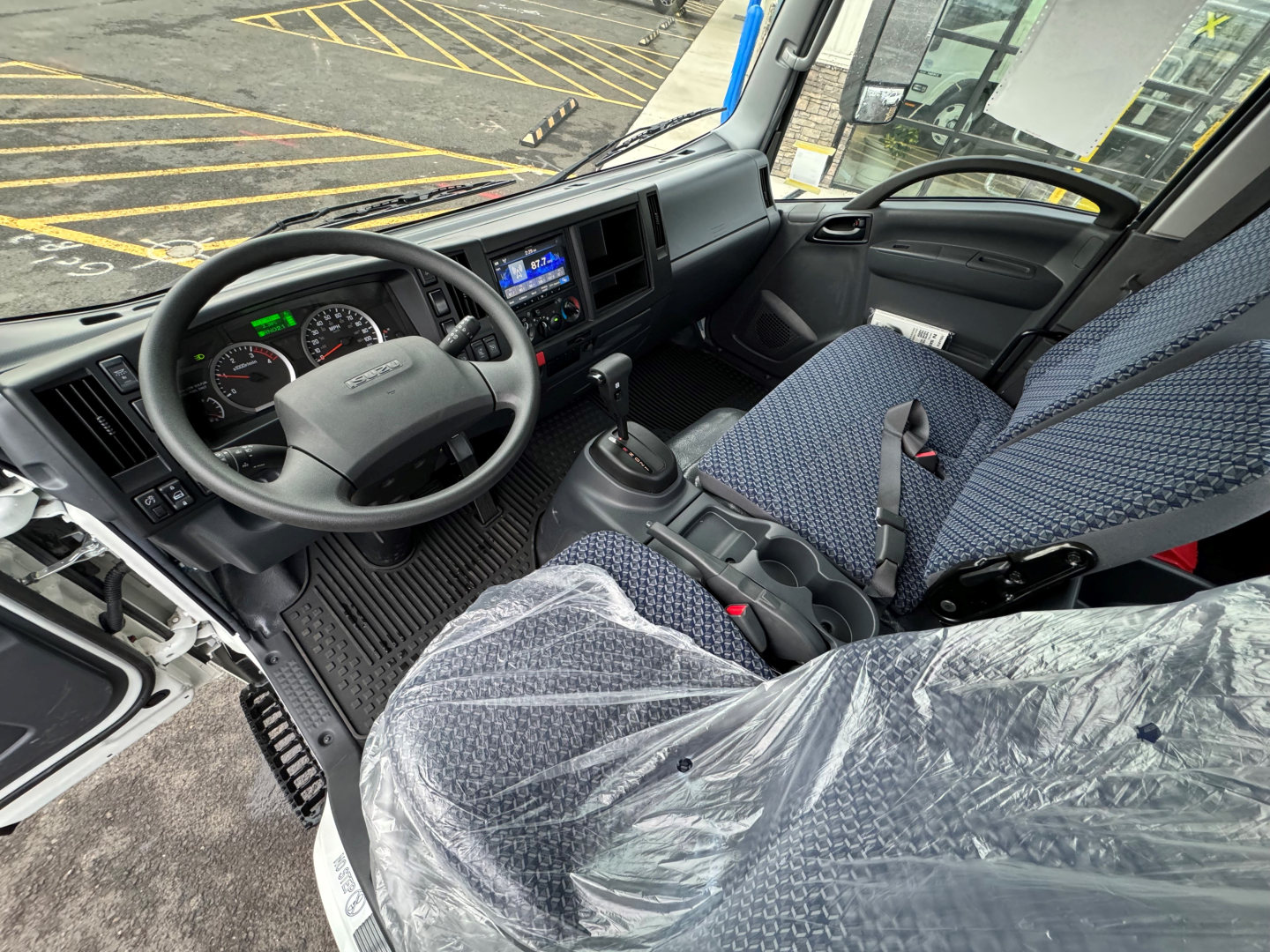 Isuzu NQR cab interior showing steering wheel dashboard gauges and front seats with protective plastic covers.