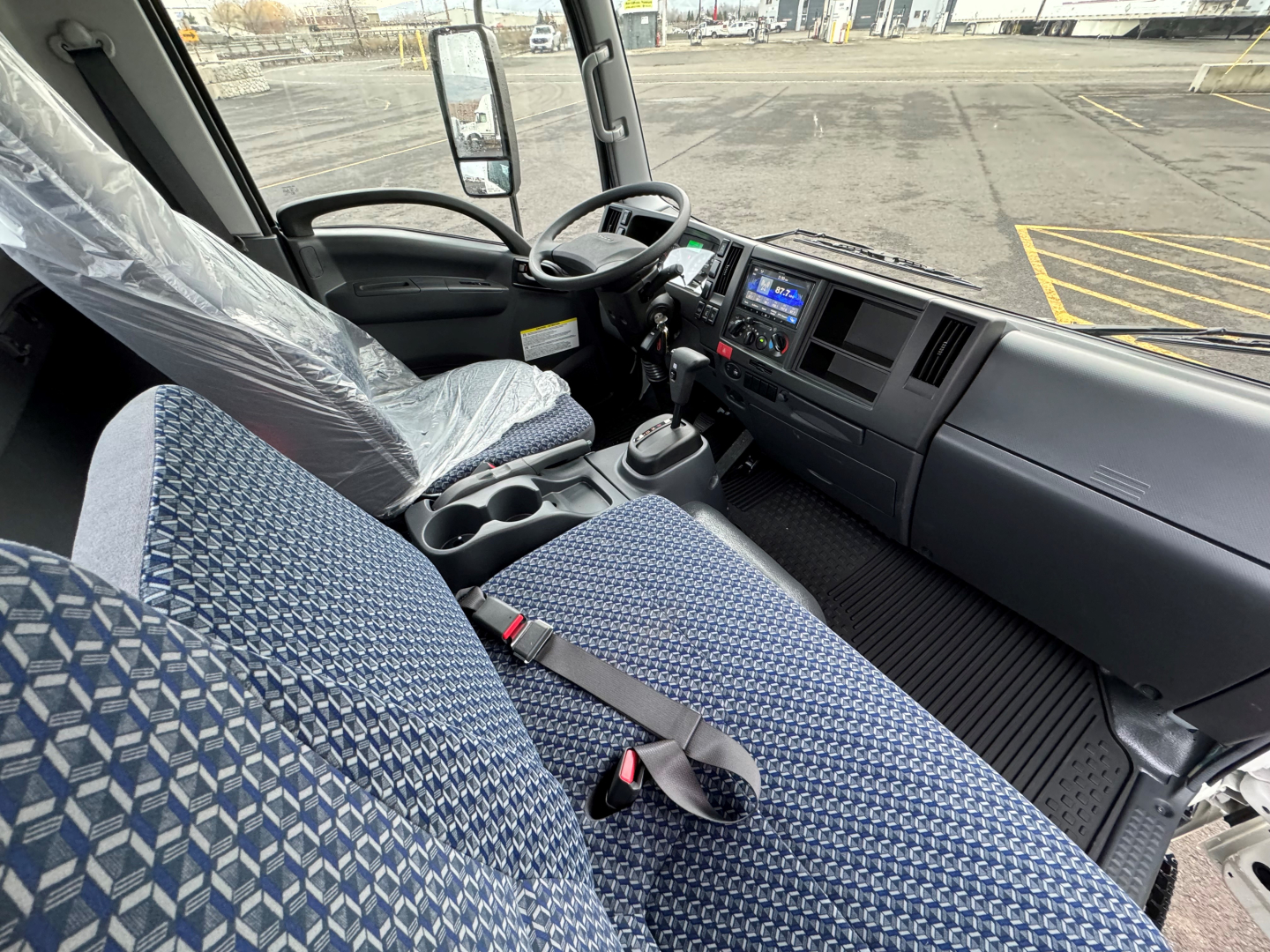 Isuzu NQR cab interior showing driver and passenger seats, steering wheel, dashboard with control screen, and gear shifter.