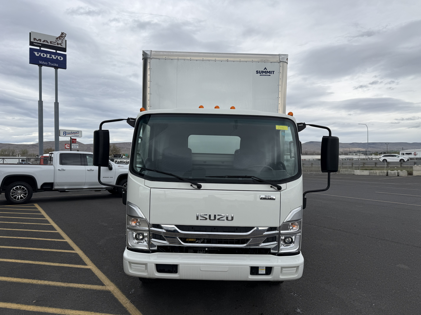 Isuzu NQR box truck front view showing cab and cargo box, with Isuzu emblem on grille and side mirrors visible.