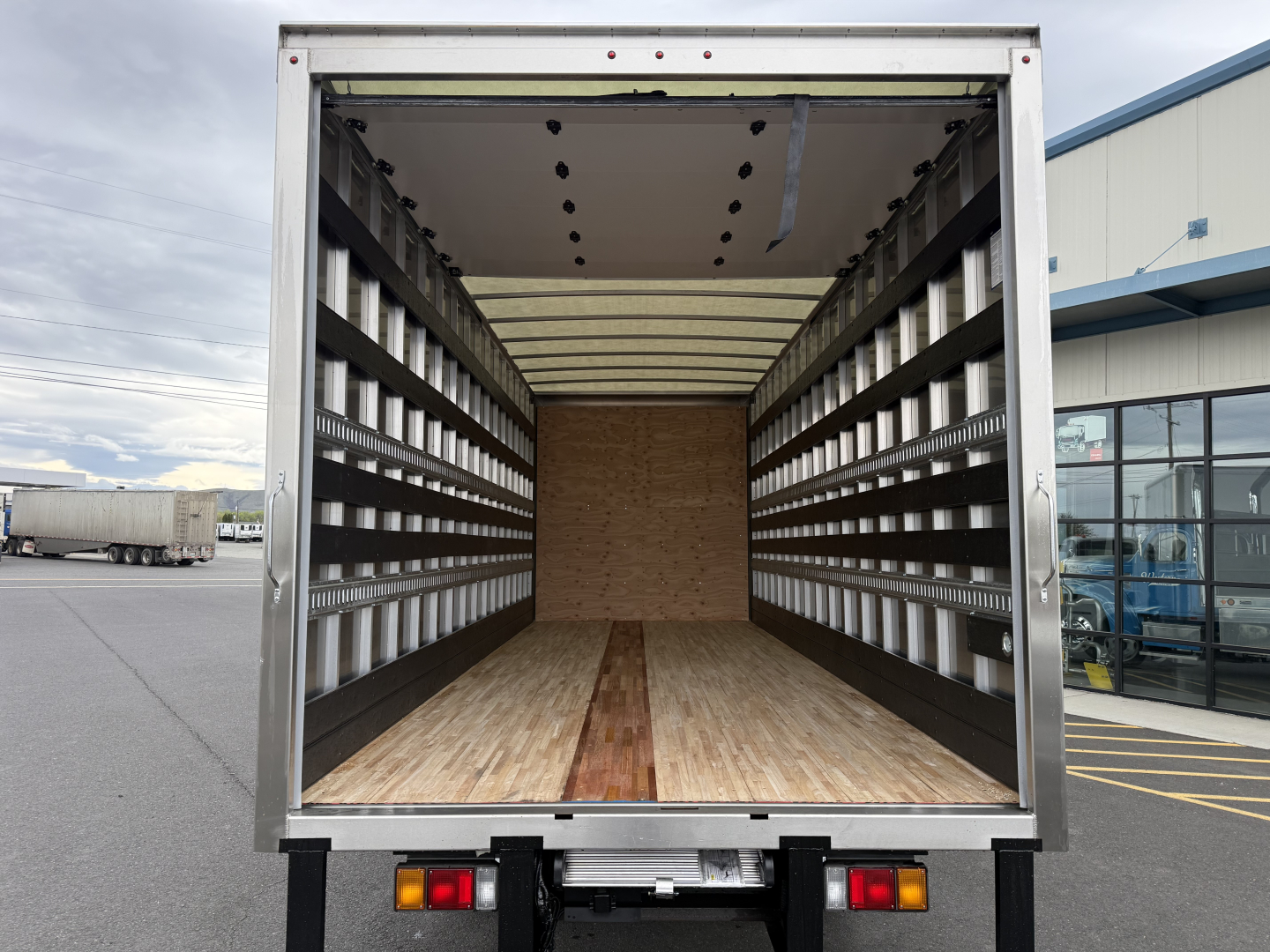 Isuzu NQR cargo truck rear with empty box interior showing wood floor, side walls with ribs and uprights, and rear bumper lights.