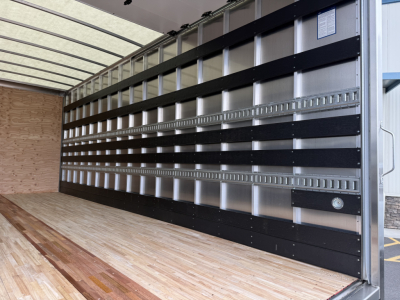 Isuzu box truck cargo area with metal sidewalls and black sill rails, empty wooden floor, interior of cargo box.