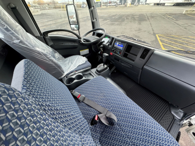 Isuzu NQR cab interior showing driver and passenger seats, steering wheel, dashboard with control screen, and gear shifter.