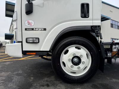 Isuzu NQR cab and chassis front wheel area showing Isuzu NQR badge and wheel, portion of cab and front bumper.