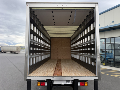 Isuzu NQR cargo truck rear with empty box interior showing wood floor, side walls with ribs and uprights, and rear bumper lights.
