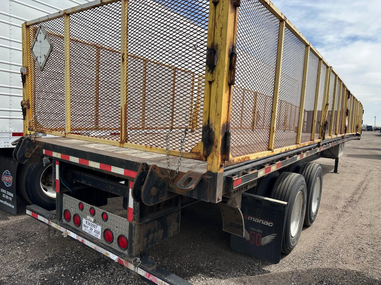 Manac closed tandem air ride steel flatbed trailer with mesh sides and dual axles, rear view showing taillights, reflectors, and wheel fenders.