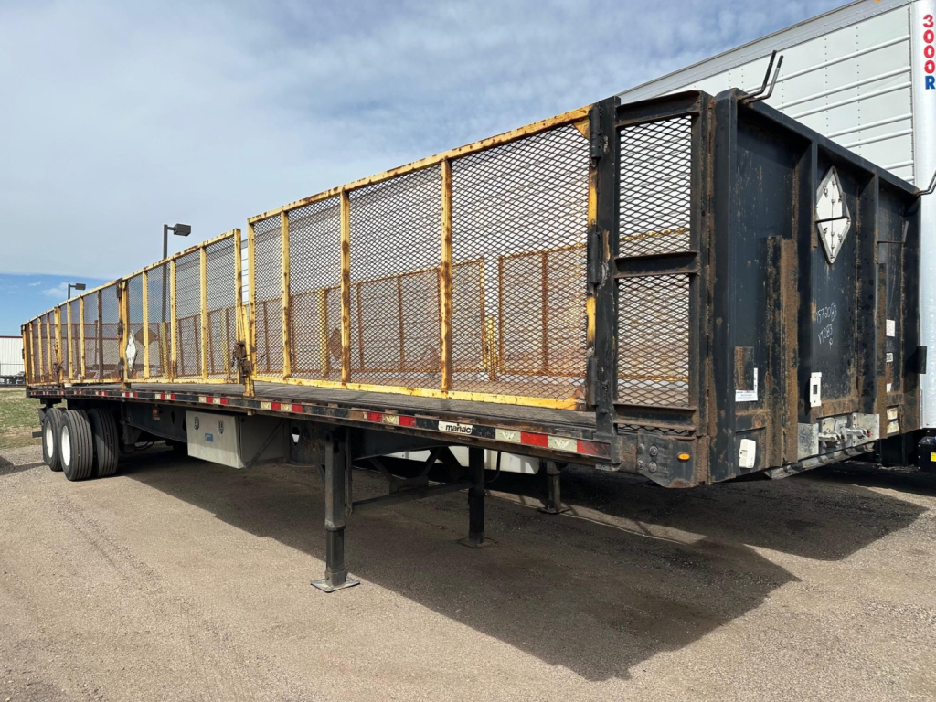 Manac flatbed trailer with closed tandem air ride, black frame and yellow mesh side gates, side view showing stake pockets and rear hitch.