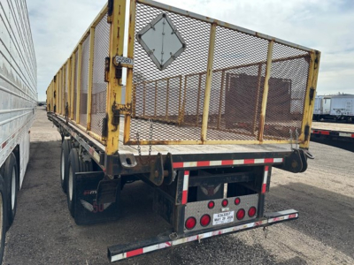 Manac closed tandem air ride steel flatbed trailer in rear view showing mesh gate and taillights.