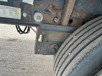 Trailer undercarriage with rusted frame showing mounting bracket and a worn tire side; label plate with small text, VIN/stock numbers not legible.