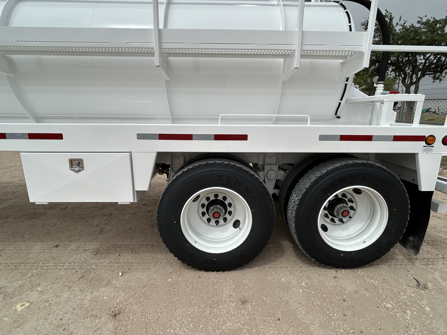Troxell 130BBL vacuum trailer side view showing dual rear wheels and storage box with small emblem; white chassis.