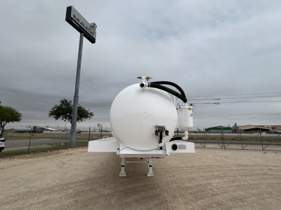 Vacuum trailer front view showing large white cylindrical tank on trailer frame with hoses and valves, sign in background.