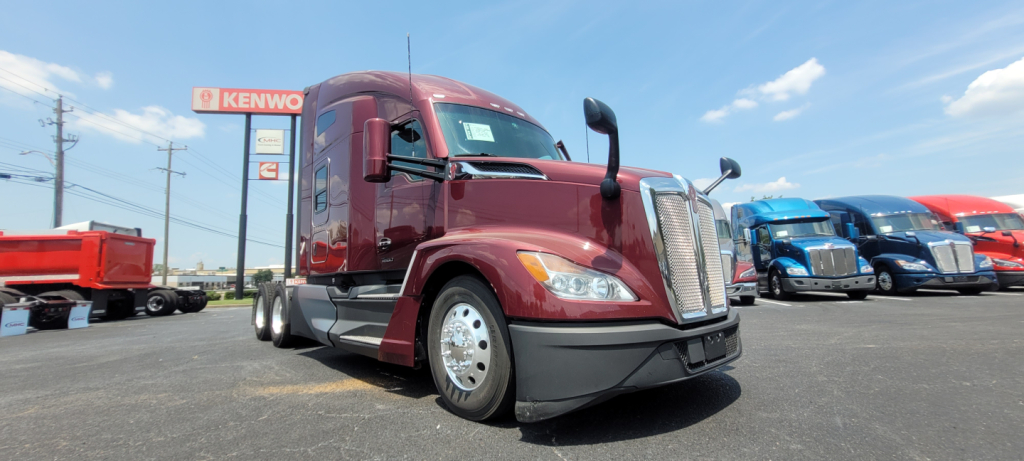 Kenworth T680 conventional sleeper truck in burgundy viewed from front-left showing chrome grille and headlights