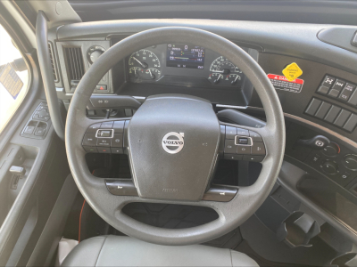 Volvo steering wheel and instrument cluster in a truck cab; dashboard displays digital screen and various controls.