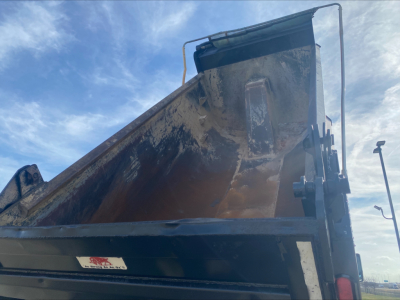 Dump truck bed with dirt and hydraulic lift, Volvo-style dump body visible.